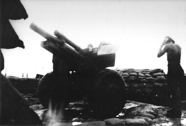 A photograph of Operation Capital, Fire Support Base.  'Flinders', a Gunner, covers his ears at 'The Fortress' or 'Sandbag City'. 