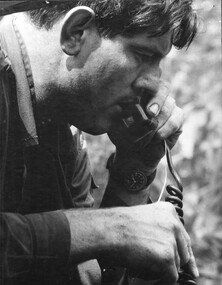 A photograph of a platoon commander with 9th Battalion, RAR, radioing map reference corrections to the forward artillery observer. 