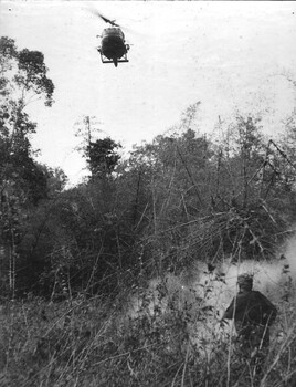 A photograph of a Digger directing a Royal Australian Air Force, 9 Squadron helicopter onto the ground after throwing smoke to reveal his position. 