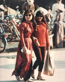 A photograph of  two local Vietnamese girls walk off to their place of work after parking their bikes in the downtown Hue. 