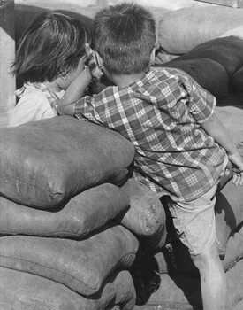 A photograph of small Vietnamese children having a tete-a-tete as they watch their respective Regional Force soldier fathers at work. 