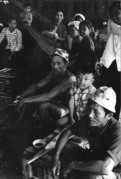 A photograph of a North Vietnamese extended family, sitting in their partially completed home at the village of Ap Sui Nge. 