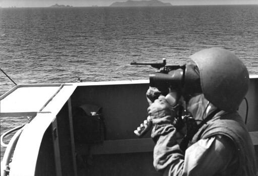 A photograph of a crew member keeping lookout on a deck of HMAS Hobart during a fire mission into Vinh, in North Vietnam. 