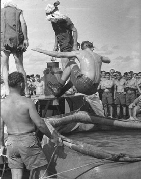 A photograph of diggers from 9th Battalion, RAR. After being 'found guilty' one is cast into the sea by courtiers of King Neptune. 