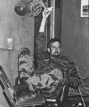 A black and white photograph of Denis Gibbons in camoflague gear taking a rest at the 1 ATF Base Nui Dat, Vietnam.