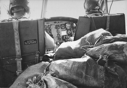 A photograph of a Royal Australian Air Force, 9 Squadron 'slick' Huey helicopter delivering a cargo of sandbagged and freshly filled water bottles.