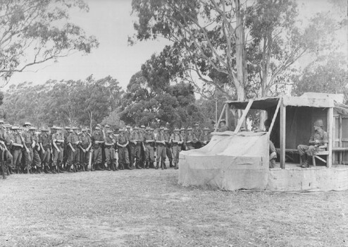 A photograph of assembled Infantry Diggers receiving instructions using a wood and hessian helicopter 'mockup' to practice embarking and disembarking. 