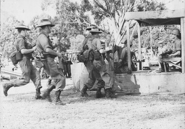 A photograph of assembled Infantry Diggers receiving instructions using a wood and hessian helicopter 'mockup' to practice embarking and disembarking. 