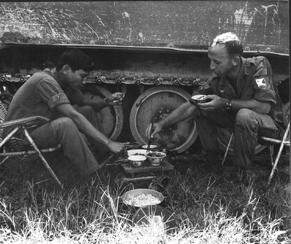 A photograph of an AATTV advisor with the Army of the Republic of Vietnam (ARVN), Armoured Corps, sharing a meal with his Vietnamese counterpart. 