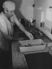 A photograph of a medic, at the 1st Australian Field Hospital, Vung Tau, cleaning instruments ready for sterilization in an autoclave machine. 