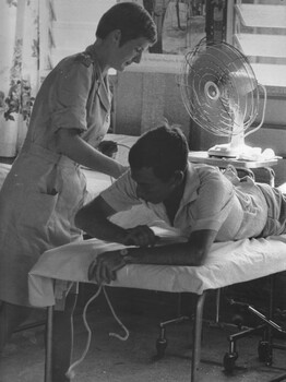 A photograph taken at the 1st Australian Field Hospital, physiotherapist Lt Sue Wooley treats a patient in the physio hut of the hospital. 