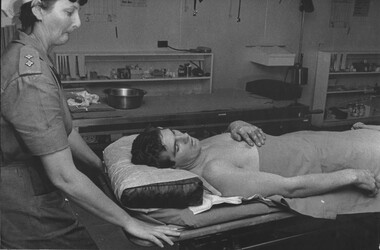 A photograph of Royal Australian Army Nursing Corps Sister Lt Desley McLean wheeling a patient from triage to the surgical ward. 