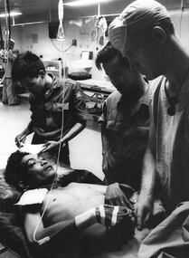 A photograph of a wounded VietCong soldier who is given some treatment by a medic, in triage, at the 1st Australian Field Hospital. 