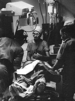 A photograph of Sister June Minchow, assisted by a medical officer and a medic, discussing a problem as she prepares a patient for surgery. 