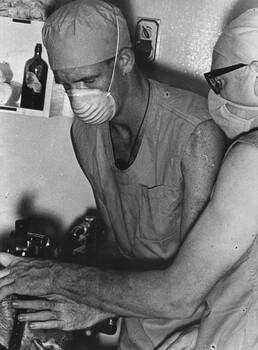 A photograph 1st Australian Field Hospital, where the Medic Corporal Alex Berry assists the anaesthetist in preparing an American helicopter pilot for the theatre. 