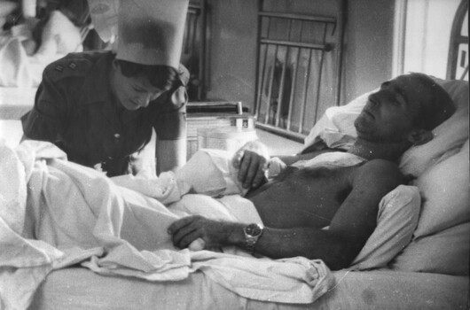 A photograph of Ward Sister Lt Ann Wright applies treatment to a wounded Special Air Services Digger Trooper Rossiter. 