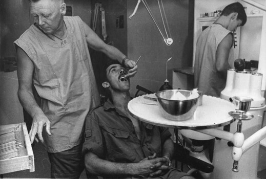 A photograph at the 1st Australian Field Hospital of a Dentist works on a Digger patient while a dental assistant mixed filling material.