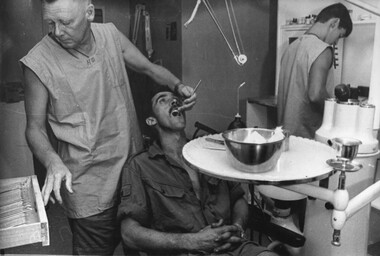 A photograph at the 1st Australian Field Hospital of a Dentist works on a Digger patient while a dental assistant mixed filling material.