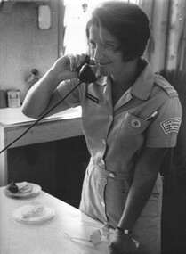 A photo of a Red Cross Staff at the 1st Australian Field Hospital, Rosemary Griggs mans the telephone in the Red Cross Hut. 