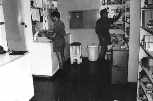 A photograph of Pharmacist Lt Roger Nation prepares prescriptions for patients in the hospital while a pharmacy assistant collects the drugs to be issued.