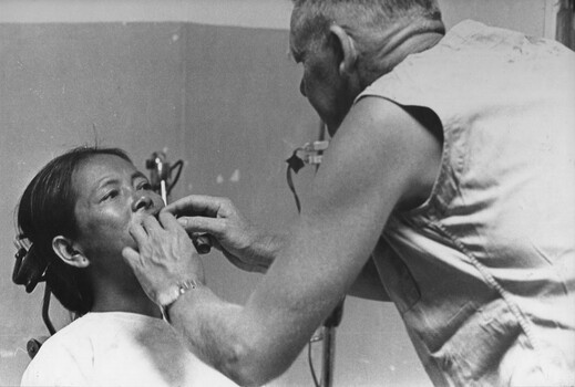 A photograph of a dentist working on a female Vietnamese patient while a dental assistant and a civilian female Vietnamese aide look on.  