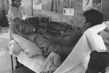 A photo of Physiotherapist Lt Diane Skewes assists a patient, while a second Digger lies face down waiting his turn for treatment.