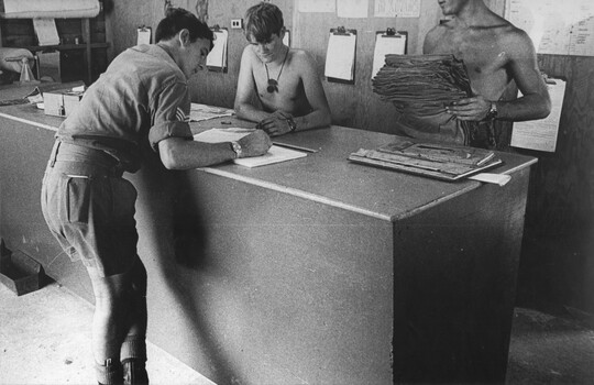 A photo at the counter of the 1st Australian Field Hospital, Quartermasters Store, Q Store staff look on as a Sergeant signs for stores. 