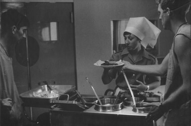 A photo of Medics Walt Darmain and Ray Yates assist Sister Lt Ruth Page at 1st Australian Field Hospital serve the evening meal. 