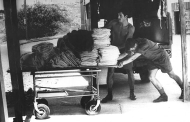 A photo of Two Medics at the 1st Australian Field Hospital strain as they push a fully laden trolley of the daily linen requirement. 