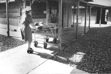 A photo at 1st Australian Field Hospital, Sr Lt Desley McLean with a Medic wheels a patient to the surgical ward.