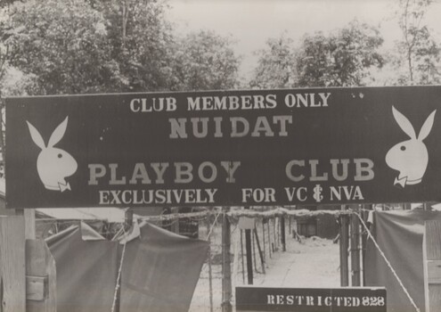 A photograph at Nui Dat  'The Playboy Club'. A sign over the entrance to the prisoner of war compound used for Nth Vietnamese army prisoners.