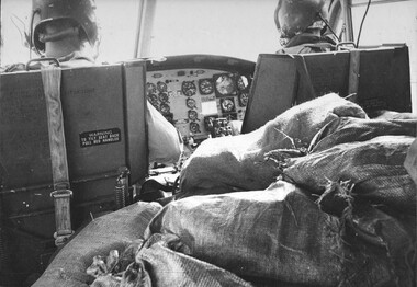 A photograph of a 9 Sqn RAAF Huey delivers a cargo of sandbagged, freshly filled water bottles to a Fire Support Base for distribution. 