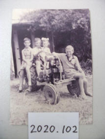 A black and white photo of James Kelly Kerr with his brothers and sisters sitting on a small tractor.