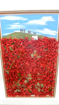 Framed painting of armed soldiers on a hill with a display of red poppies below. Poppies are fabric.