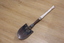 Small metal round nose shovel with white wooden handle. A twisting mechanism between metal and wood allows the item to fold.
