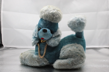 Image of stylised poodle toy with two-toned blue fur. Dog is looking to side and in crouched/lying position.