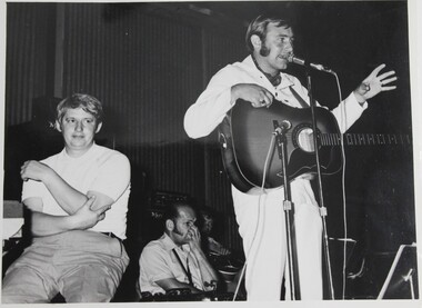 A sepia photo with the ABC showband in the background at Christmas 1970 with Brian May and comedian Ray Gibson.