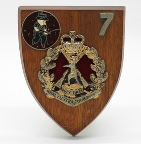 Wooden shield-shaped plaque with metal badges of the pig emblem of 7th Battalion Royal Australian Regiment(RAR) and the official RAR emblem.