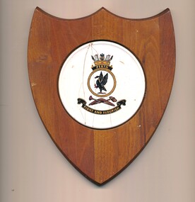 Wooden shield with white ceramic circle inset featuring the emblem and motto of the HMAS Perth.