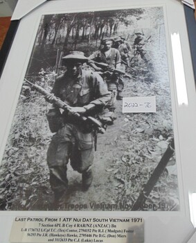 Black and white photograph featuring five soldiers in full battle gear making their way through the jungle. 