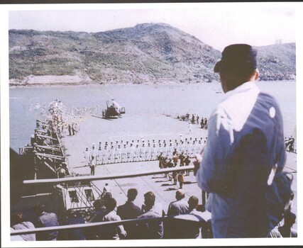 HMAS Sydney anchored in Vung Tau in 1968. A pipe band playing behind navy soldiers in rank facing a HUEY.