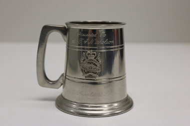 A pewter tankard with dedication to TJ Nicholson, and a raised insignia of Armoured corps and four etched bands around circumference.