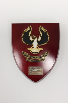 A reddish wooden plaque featuring a black and white bird with outspread wings, presented to T Nicholson from PMC And Members December 1989.