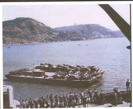 Colour photograph of HMAS Sydney showing landing boats ferrying equipment with army personal on deck.