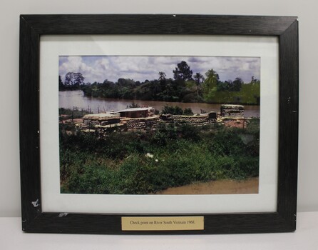 A framed coloured photograph of a check point on a river bend.