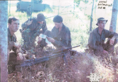 A laminated copy of a coloured photograph of four soldiers sitting on the ground