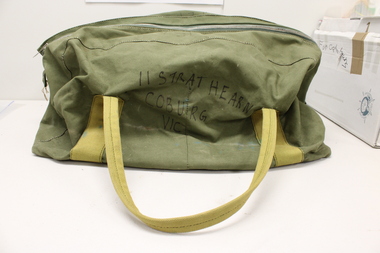 A green army duffle bag with mustard coloured handles