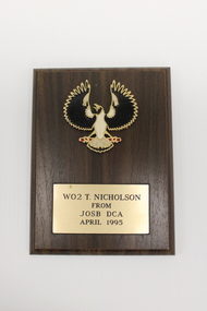 Rectangular wooden plaque featuring a black and white bird with outspread wings and a rectangular engraved plaque beneath it.