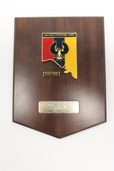 Wooden plaque with red, blue, yellow, black, white and gold insignia of DSU Adelaide 