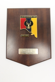 Wooden plaque with red, blue, yellow, black, white and gold insignia of DSU Adelaide 